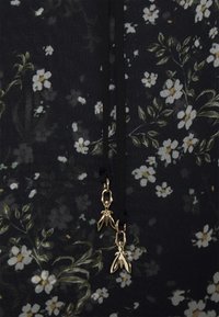 Un tissu à motif floral noir présente des fleurs blanches et des feuilles vertes. Deux charms en forme d'insecte doré sont fixés au cordon de serrage.