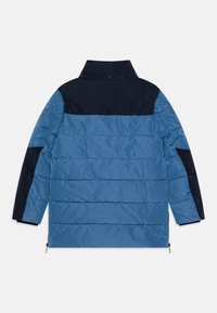 Mėlynas ir tamsiai mėlynas pūkinis džemperis su aukštu apykakle, horizontaliu siuvinėjimu ir užtrauktukais šoninių siūlių apačioje. Vandeniui nepralaidus medžiaga.