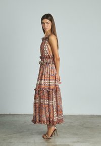 Abito maxi in tessuto stampato, caratterizzato da toni terrestri e ruches, design senza maniche, con vita stretta e gonna a strati.