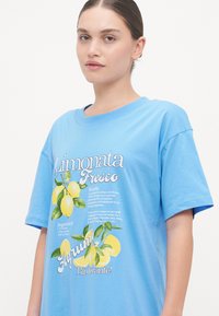 T-shirt azzurro chiaro a maniche corte con una grafica di limoni e testo in italiano. Realizzato in morbido cotone, con una vestibilità rilassata e scollo rotondo.