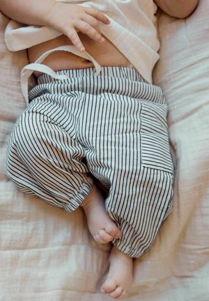 Bébé allongé portant un pantalon à rayures blanches et noires avec un cordon et une poche, montrant les mains, les pieds et le ventre.