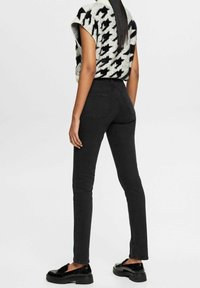 Jeans negros de cintura alta con un corte ajustado, que cuentan con bolsillos traseros. Combinados con un suéter de gran tamaño en gris y negro con un patrón y zapatos negros.