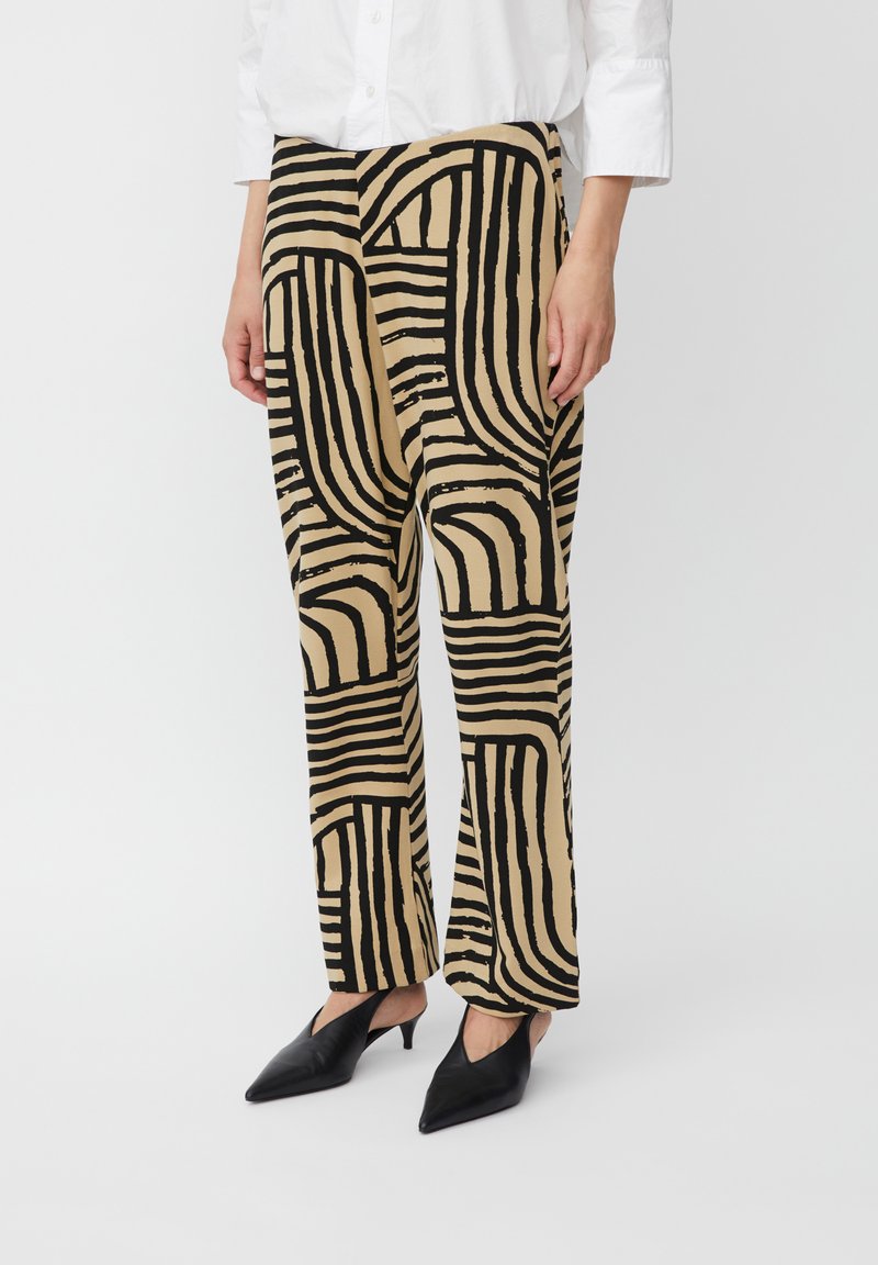Pantalons larges beiges avec des rayures abstraites noires. Fabriqués dans un tissu léger, avec une taille haute et une coupe décontractée.