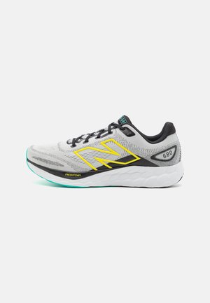 Zapatilla deportiva gris con acentos negros y logo amarillo. Presenta una parte superior de malla transpirable, suela blanca acolchada y detalles texturizados.