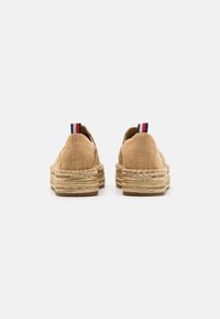Espadrilles en toile de couleur beige avec des semelles en jute tressé ; dotées d'un onglet au talon rouge, blanc et bleu et d'un design à dos fermé.