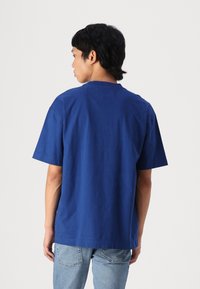 Blue cotton T-shirt with short sleeves and a crew neckline, featuring a smooth texture and relaxed fit, paired with light-wash denim.