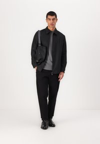 Sort tætsiddende jakke med smalle striber over en grå sweater, parret med sorte bukser og ankelstøvler. En lille sort crossbody taske fuldender looket.