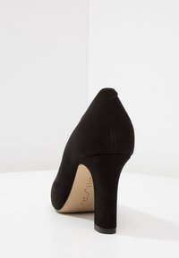 Black suede high heel shoe with a pointed toe and a tapered heel. The sole is black, and the inner lining is beige with branding visible.