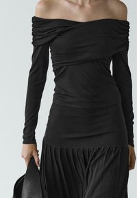 Top nero scollato con maniche lunghe, caratterizzato da tessuto drappeggiato e design aderente, abbinato a una gonna plissettata.