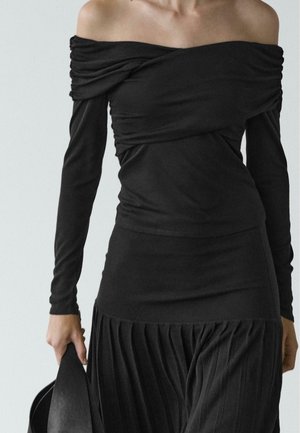 Top nero scollato con maniche lunghe, caratterizzato da tessuto drappeggiato e design aderente, abbinato a una gonna plissettata.