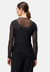 Haut noir à manches longues en matériau transparent avec un ourlet festonné et un encolure arrondie à l'arrière. Design épuré avec une silhouette ajustée.