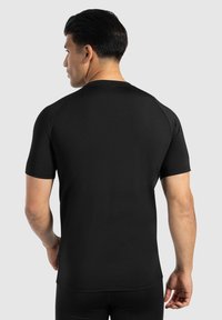 Schwarzes kurzärmeliges Sportshirt aus glattem, dehnbarem Stoff mit Rundhalsausschnitt und Raglanärmeln, das eine taillierte Passform zeigt.