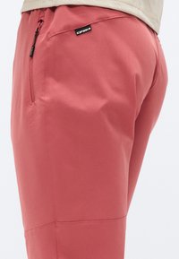 Ροζ αθλητικό παντελόνι από ελαφρύ ύφασμα, με φερμουάρ σε τσέπη στη δεξιά πλευρά και εμφανείς λεπτομέρειες ραφής.
