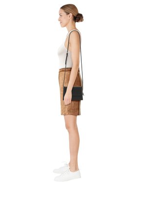 Woman with hair in a bun wears a white tank top, brown suede skirt, white sneakers, and carries a black crossbody purse on her shoulder.
