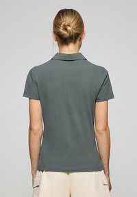 Grå pikétröja med krage, korta ärmar och en slät yta, sedd bakifrån. Tröjan har en ren, passande design.