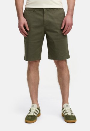 Olijfgroene katoenen shorts met een rechte pasvorm, voorzakken en een zoom die net boven de knie eindigt. Gecombineerd met groene en crèmekleurige sneakers.