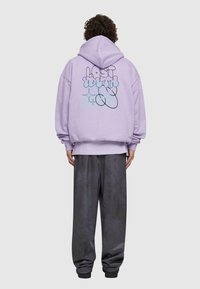 Felpa lavanda con una grande grafica astratta sul retro in toni di nero e blu, abbinata a pantaloni grigi larghi con polsini elastici.