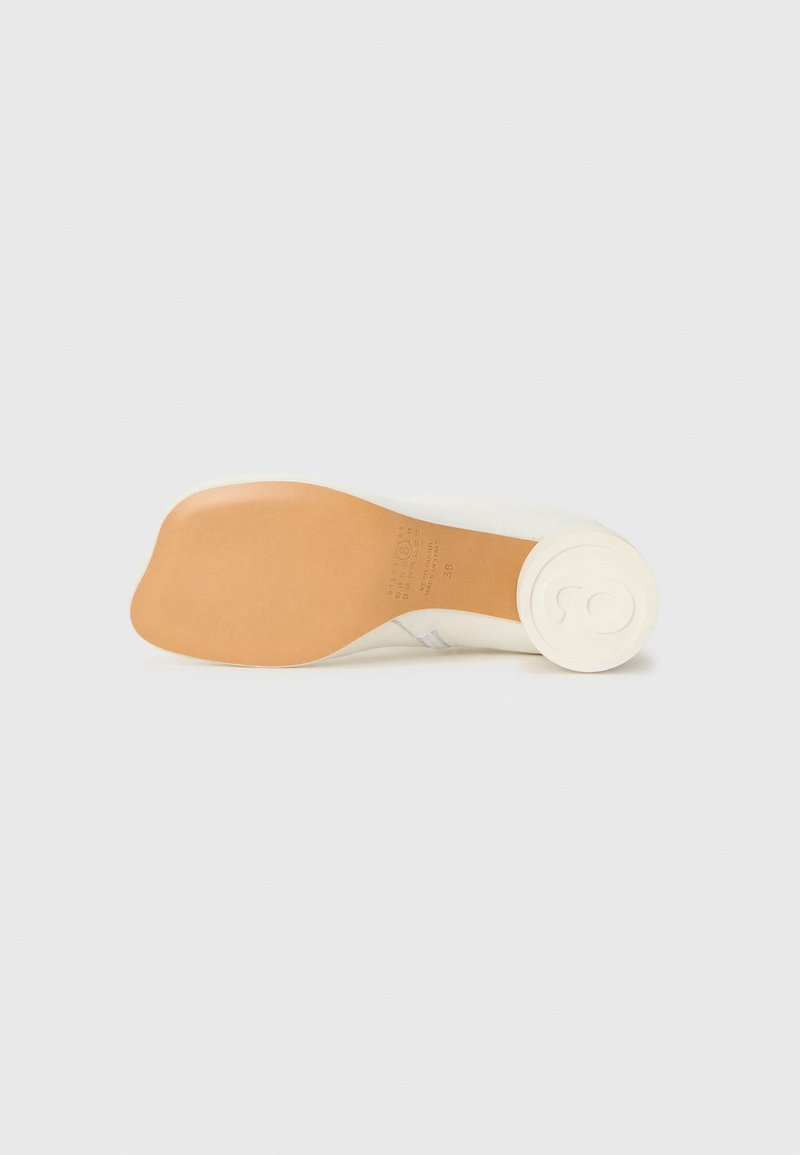 Scarpa color crema con suola in gomma, caratterizzata da una texture liscia e un tacco arrotondato. La parte inferiore mostra un logo impresso e le indicazioni della misura.