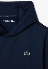 Mörkblå hoodie i mjukt material, med en framficka, rundad halsringning och en liten broderad krokodillogo på bröstet.