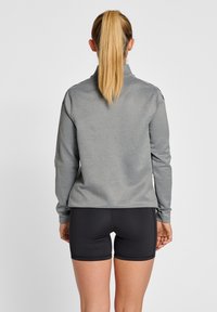Grå långärmad topp med hög krage och åtsittande ärmar, kombinerad med svarta sportshorts. Slät textur, minimalistisk design, inga synliga mönster.