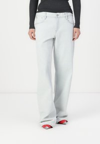 Jeans de tiro alto, de pierna ancha y color azul claro, con cinco bolsillos y un botón de metal. Combinados con zapatos rojos de punta y un suéter negro acanalado.