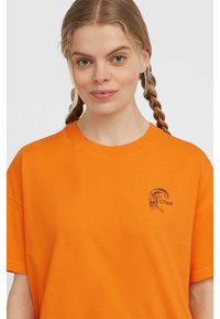 Oranžové bavlněné tričko s volným střihem a krátkými rukávy. Na hrudi má malé černé grafické logo. Hladký povrch.