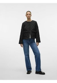 Juodas pamuštas švarkas su apvaliu kaklu, mygtukų uždarymu ir dviem priekinių kišenių, derinamas su mėlynomis plačiomis kelnėmis ir juodais batais.