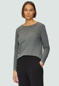 Een langemouwen shirt van een zachte grijze stof met een ronde halslijn en een ontspannen pasvorm, gecombineerd met zwarte broeken met een zijzak.