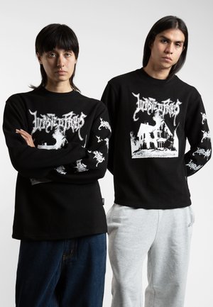 Chemises noires à manches longues avec des imprimés graphiques sur le devant et les manches, en tissu texturé. Un mannequin porte un pantalon de survêtement gris clair.