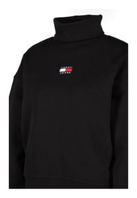 Felpa nera con colletto alto, caratterizzata da una piccola toppa del logo TOMMY JEANS in rosso, blu e bianco. Realizzata in morbido tessuto testurizzato.