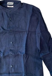 Camicetta di lino blu navy con colletto alla mandarino, patta dei bottoni e maniche lunghe. Texture morbida con trama del tessuto visibile e lievi pieghe.