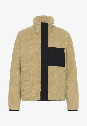 Veste en polaire sherpa beige avec col haut, couverture de fermeture éclair noire à l'avant et poche poitrine zippée noire.