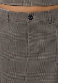 Bézs kockás nadrág, szövetből készült, fekete gombbal, öt zsebbel és strukturált derékkal.