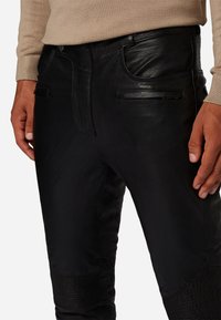 Zwarte leren broek met gedetailleerde stiksels, verhoogde texturen op de kniezones en subtiele zakken, ontworpen voor een aansluitende silhouet.