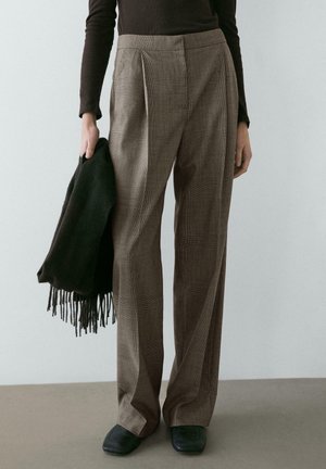 Hnědé kostkované kalhoty s vysokým pasem a záhyby, doplněné tmavě zeleným šátkem a tmavými botami. Hladká textura s upraveným střihem.