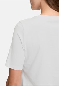 Biała koszulka z krótkim rękawem o gładkiej fakturze i prostym wzorze. Widok z tyłu ukazuje zaokrąglony dekolt i luźny krój.
