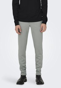 Jasnoszare slim-fit spodnie z elastycznego materiału, z płaskimi szwami i gładką teksturą, w połączeniu z czarnymi skórzanymi botkami.