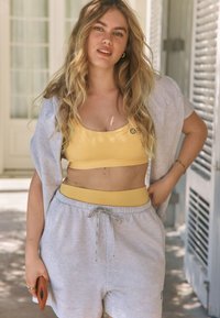 Sárga crop top és magas derekú szürke rövidnadrág húzózsinórral. A modell világosszürke, túlméretezett kardigánt visel és telefont tart a kezében.