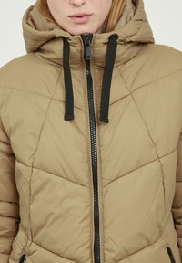 Beige prošívaná bunda s kapucí, zipem a černými šňůrkami. Hladký materiál, střední délka.