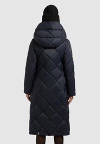 Geacă puffer bleumarin cu model quadrat în diamond, glugă supradimensionată, mâneci lungi și un design de lungime medie. Asortată cu o bonetă tricotată neagră.