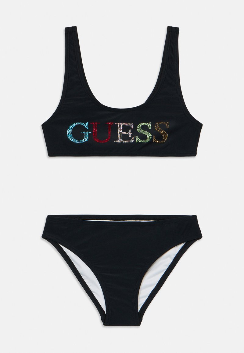 Juodas bikini komplektas su apvaliu iškirpimu, kuriame yra spalvingas kalnų krištolas „GUESS“ logotipas ir atitinkami žemi šortukai su balta pamušalu.
