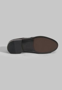 Bruine schoenzool met een gestructureerde zwarte rubberen hiel, met een gladde bruine onderkant en subtiel grippatroon, ontworpen voor comfort en stabiliteit.