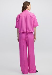 Roze tweedelig outfit bestaande uit een kort mouwloos, los shirt met een trekkoord in de taille en wijde broekspijpen. Glad, lichtgewicht stof.