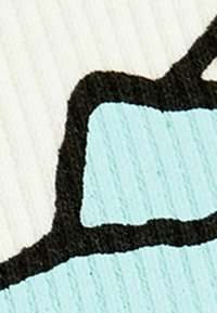 Tekstilpatch med en lys blå form, omkranset af sort, på en struktureret hvid baggrund, der fremhæver kontrast og designelementer.