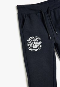 Marineblaue Sweatpants mit geripptem Bund, Kordelzug, zwei seitlichen Taschen und weißem Grafiktext "Harajuku Street Fashion 82 Tokyo-JPN."