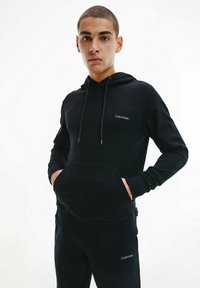 Felpa nera realizzata in materiale morbido, con tasca frontale, cappuccio con cordino e piccolo logo bianco di Calvin Klein sul petto.