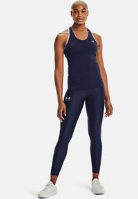 Marinblå trenings tanktop med hvite stropper, kombinert med marinblå kompresjonsleggings med et subtilt mønster og Under Armour-logo.