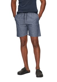 Shorts de style denim d'un bleu moyen, avec une taille élastique et un cordon de serrage, ainsi que des poches latérales. Associés à des chaussures noires à enfiler.