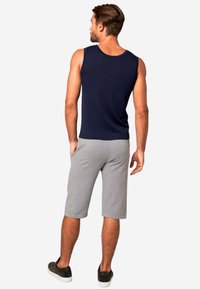 Canotta senza maniche di colore blu navy abbinata a pantaloni corti grigi fino al ginocchio. Indossata con scarpe slip-on nere, che mettono in mostra un look atletico casual.