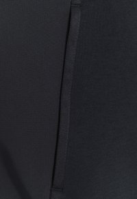 Haut de sport noir présentant un tissu texturé à finition lisse, souligné par une sangle verticale le long du côté.